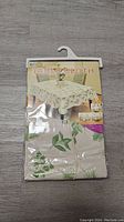 Front view of packaged table cloth showing product image with botanical pattern and size info.