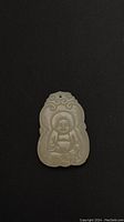 Front view of light green jade Buddha pendant showing detailed carving and hole for stringing.