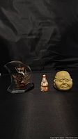Photo displaying the three items against a black fabric background: clear acrylic base with owl figurine, small ceramic Buddha, beige clay head sculpture.