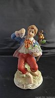 Front view of the porcelain figurine of a boy holding grapes and a fruit basket, showing detailed facial features and vibrant clothing colors.
