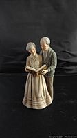 Front view of the porcelain figurine showing the elderly couple reading a book, detailed craftsmanship visible, signed piece.