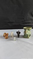 Five elephant figurines including green ceramic planter and four smaller carved stone or resin figurines shown on a white surface with black background.