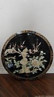 Full front view of the round black lacquer wall art with mother of pearl inlay featuring birds and flowers.