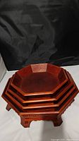 Stack of four nested octagonal wooden plates in reddish-brown color, side view showing depth and tenon joinery style.