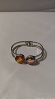 Silver-tone bracelet featuring two round end pieces: one with the Wonder Woman logo on red background, and the other with an illustrated Wonder Woman image.