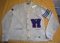 Full view of the front of the vintage letter sweater showing the overall condition, including spots and holes, the button front, and the striped sleeve.