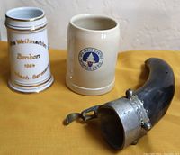 Three drinkware items: two ceramic beer steins and one horn-shaped drinking horn with metal top.