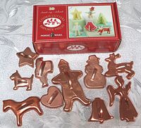 Photo showing multiple copper colored vintage cookie cutters including animals, stars, hearts, and bells with the Nordic Ware 3D stand-up set box in the background.