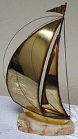 Angle view of brass sailboat sculpture on marble base showing curved polished brass sails, a flag, and the base's coloration.