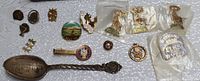 Top-down image showing spoon, jewelry box, and multiple pins including 14K pin, Elks pins, and other organizational pins on white fabric.