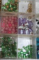 Close up view of six bead compartments showing texture, colors, and shapes of beads including matte pink, green, purple beads with designs, and gold metal beads.