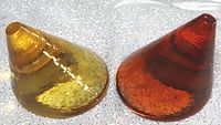 Photograph of two cone-shaped glass paperweights, one amber yellow and the other deep amber/red, showing top and side view with surface and internal bubbles.