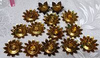 14 flower-shaped brass candleholders arranged with visible wax remnants and oxidation spots, top view.