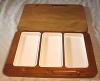 Photo of the open wood cheese board showing three white plastic compartments inside for cheese, meat, or olives.