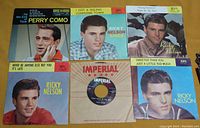 Top-down photo of all six 45 RPM vinyl records, including Perry Como and Ricky Nelson with one plain Imperial sleeve visible.