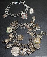 Photo of two silver charm bracelets on black background showing multiple unique charms including Southwestern and themed pieces