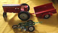 Metal red tractor with attached red trailer and green plow attachment in front. Tractor marked Tru Scale.