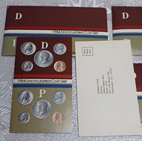 Four 1984 US Mint uncirculated coin set envelopes including 'D' and 'P' mint marks, pamphlets, and survey card on white surface.