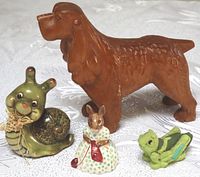 Carved wooden dog and three ceramic/plaster animal figures on a white textured surface