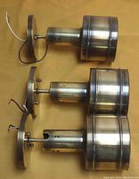 Top view of three mid-century ceiling or wall swivel spotlight lamps arranged horizontally showing brassy metal finish and attached wiring.