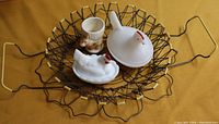 Photo showing two white milk glass hen dishes, a ceramic rabbit egg cup, and wire egg basket on a brown surface