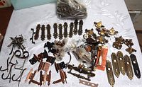 Full layout of various vintage hardware including drawer pulls, hinges, doorplates, and hooks spread out on fabric surface.