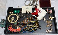 Tray with assorted vintage costume jewelry including earrings, necklaces, brooches, bracelets, and an empty watch box