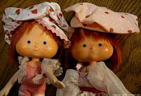 Two vintage Strawberry Shortcake dolls wearing strawberry-themed hats and detailed outfits with striped stockings.