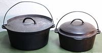 Two Wagner Ware cast iron pots side by side, one large with chipped lid and bent handle, smaller in good condition