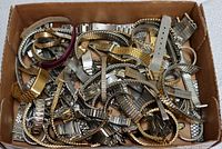 Top view photo showing a large lot of mixed metal watch bands with some leather bands on top in a cardboard box.