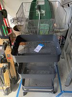 Black three-tier metal mesh storage cart with wheels, placed in a garage setting