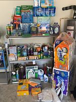 Overall view of a four-tier metal shelving unit holding assorted cleaning products and paper goods