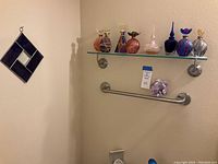 Display of eight colorful glass perfume bottles on glass shelf mounted on wall, with purple and white glass ornament and geometric purple leaded glass wall piece nearby