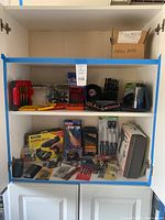 Full view showing both shelves of the cabinet containing multiple tool items including drill bits, glue gun, screwdrivers, and packaging boxes