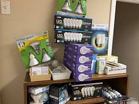 Wide view of assortment of light bulbs including CFL, LED multi-packs, and others stacked on a wooden surface.