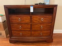 Front view of dresser showing curved front, five drawer fronts with silver ring pulls and two open shelves.