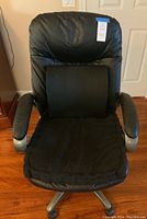Front view of black leather desk chair with black cushions on the seat and backrest. Chair has padded armrests.