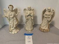 Front view of the three Lenox angel figurines together, showing their distinct poses and embellishments on robes and halos.