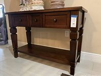 Sideboard table from a side angle showing three drawers and the lower shelf, dark brown wood.