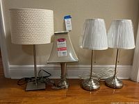Four table lamps side by side showing various bases and lamp shades.