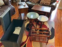 Overview of fabric storage chest with open lid, wooden tables including magazine table, charging console table, and trio of nesting tables with dark wood and marble tops.