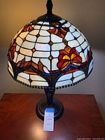 Front view of Tiffany style lamp showing stained glass shade with floral and geometric design on wooden table.