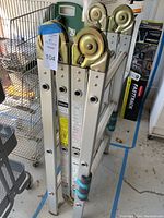 Side view of folded VersaLadder showing multiple hinges and wheels, with visible blue and black rubber feet grips.