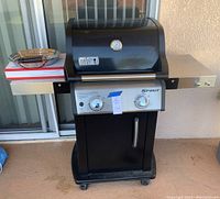Front view of the Weber Spirit gas grill showing grill lid, control panel, and side shelves with grilling accessories on left shelf.