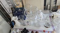 Overview of multiple glass and crystal items including cake pedestal, vases, and bowls on a table.