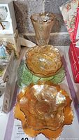 View of carnival glass marigold ruffled bowls and green depression glass plate, displayed on shelf.