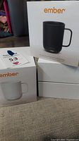 Two Ember temperature controlled ceramic mugs in original branded boxes, one black and one white, shown from the outside.