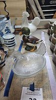 Photo of all three bird figurines including the white milk glass rooster and hen and the painted ceramic duck on a wooden table with other items