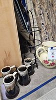 Photo showing 4 drip mugs, metal plate holder, and floral pitcher on floor.