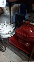 Shelf with two soup tureens: white ceramic with fruit design and red hexagonal ceramic tureen with lid and tray